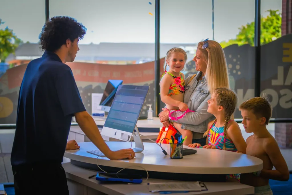 a family checking in at the front desk with a staff member before their swim lesson