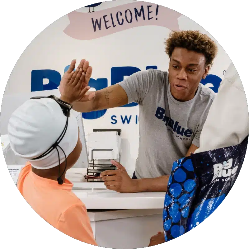 front desk staff at Big Blue Swim School giving a student a high-five