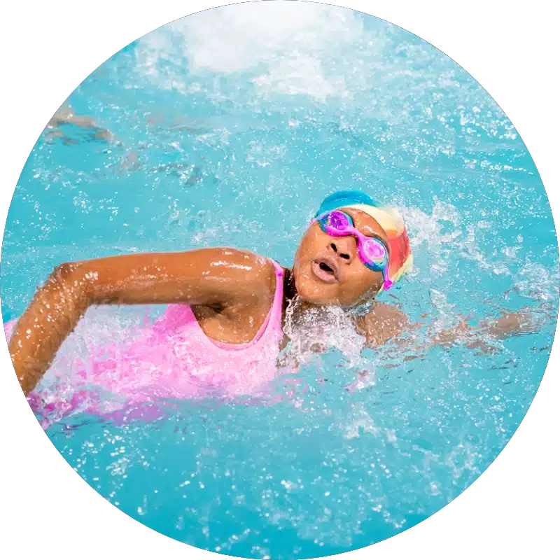 a swimmer wearing a pink swimsuit, pink goggles, and a swim cap is practicing their front stroke during a swim lesson