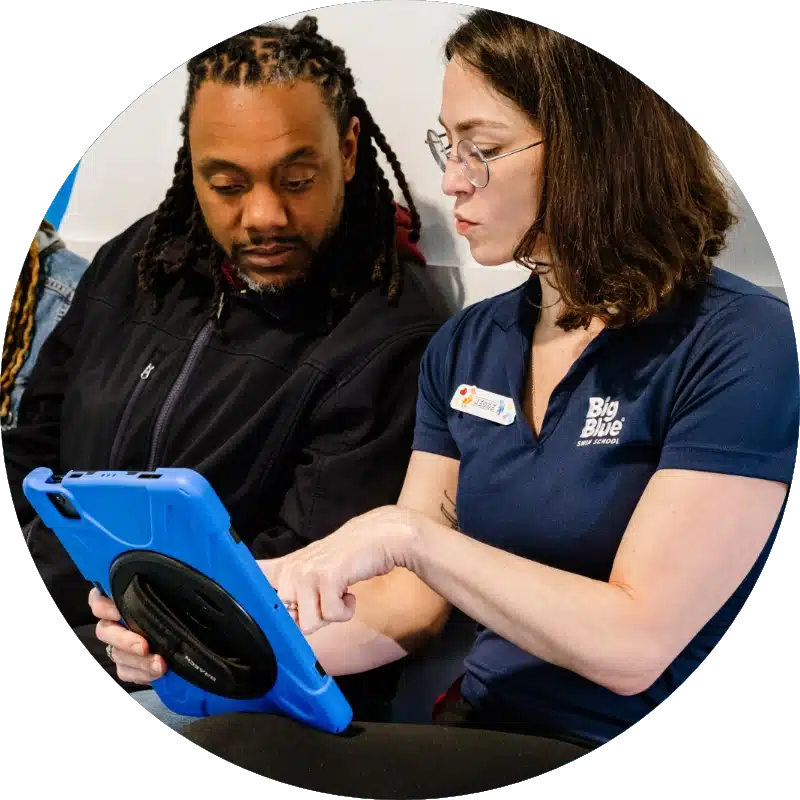 staff member showing a dad more about scheduling swim lessons on a tablet
