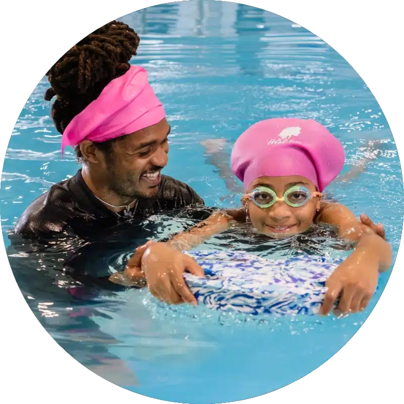swim instructor helping a child swim with a kick board during a swim lesson