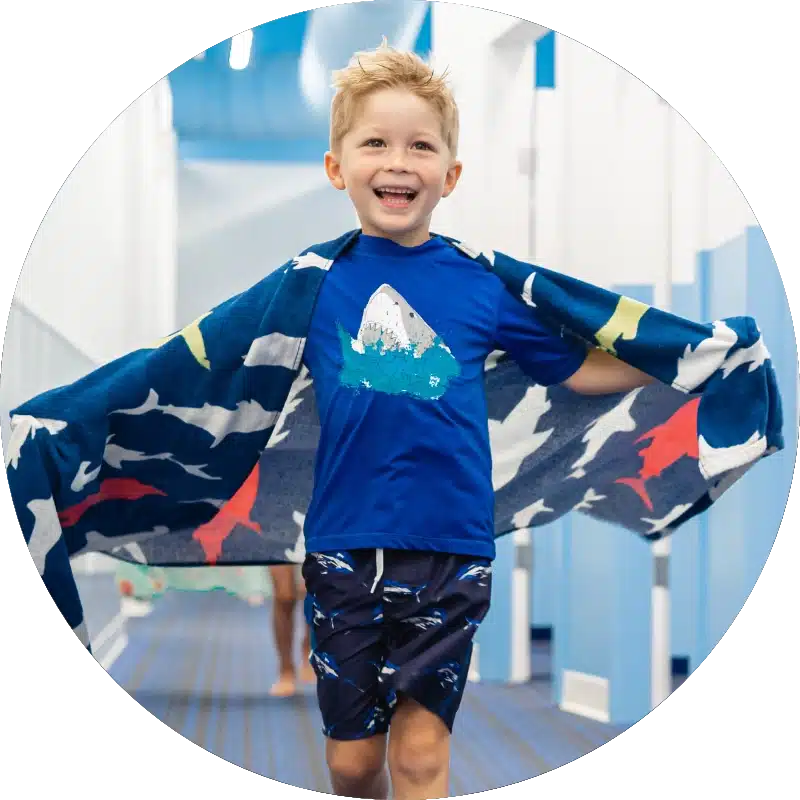smiling kid using a towel as a cape after a swim lesson